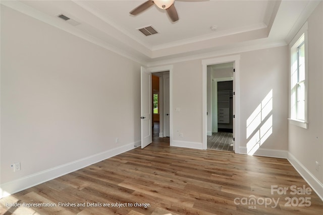 empty room with wood finished floors, visible vents, a ceiling fan, and a tray ceiling