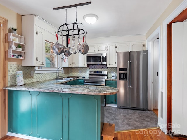 kitchen featuring pendant lighting, sink, appliances with stainless steel finishes, white cabinets, and kitchen peninsula