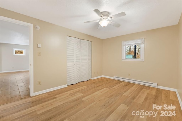 unfurnished bedroom featuring baseboard heating, ceiling fan, a closet, and light hardwood / wood-style floors