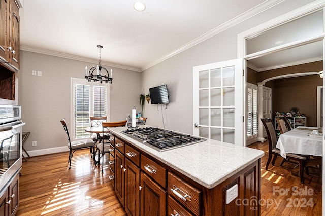 kitchen featuring appliances with stainless steel finishes, light wood-type flooring, ornamental molding, decorative light fixtures, and a kitchen island