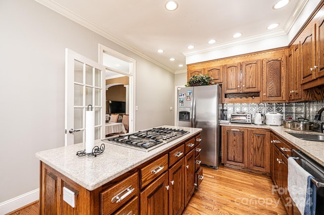 kitchen with appliances with stainless steel finishes, backsplash, sink, light hardwood / wood-style floors, and a kitchen island