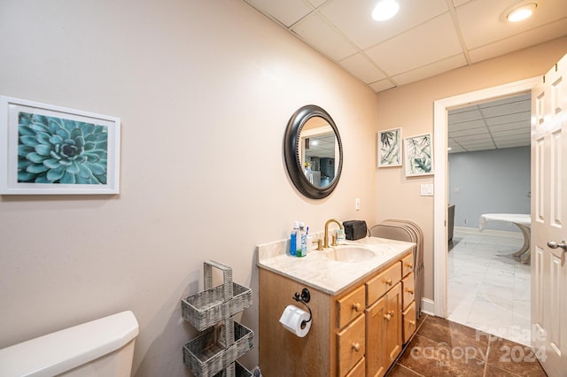 bathroom featuring vanity, toilet, and a drop ceiling