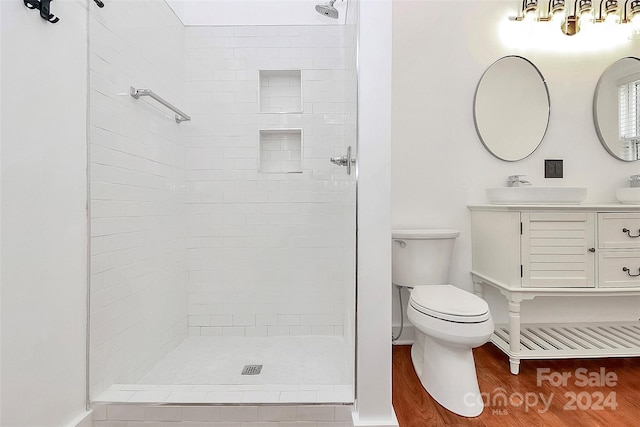 bathroom with a tile shower, vanity, wood-type flooring, and toilet