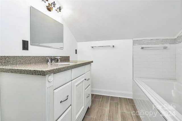 bathroom with wood-type flooring, vanity, tiled bath, and lofted ceiling