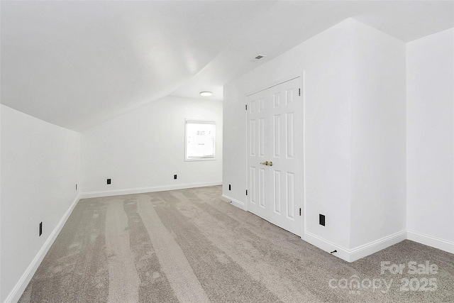additional living space with baseboards, visible vents, vaulted ceiling, and light carpet