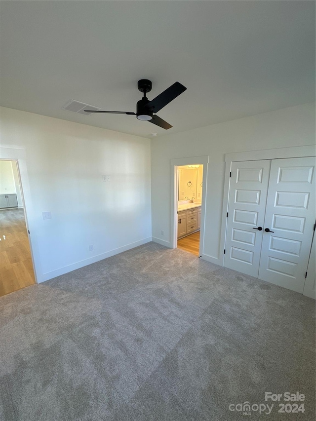 unfurnished bedroom with a closet, ensuite bath, ceiling fan, and light colored carpet