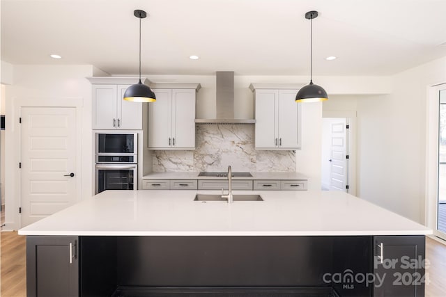 kitchen featuring white cabinetry, wall chimney exhaust hood, a large island with sink, pendant lighting, and wood-type flooring