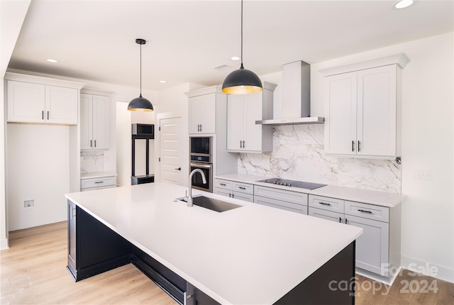 kitchen with a center island with sink, wall chimney exhaust hood, light hardwood / wood-style floors, and black electric stovetop