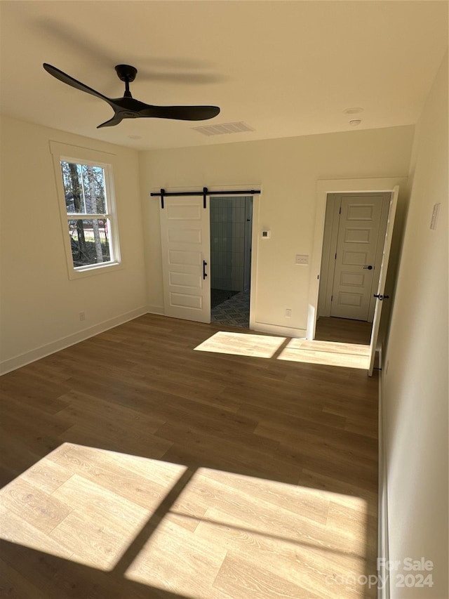 empty room featuring dark hardwood / wood-style flooring, a barn door, and ceiling fan