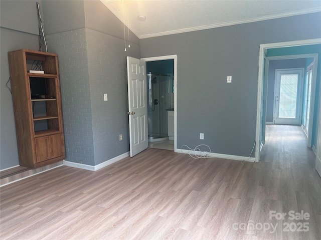 interior space with lofted ceiling, ornamental molding, light hardwood / wood-style floors, and brick wall