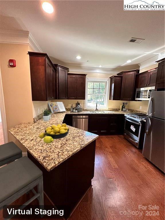 kitchen featuring light stone countertops, dark wood-type flooring, stainless steel appliances, kitchen peninsula, and a kitchen bar