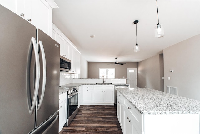 kitchen featuring sink, appliances with stainless steel finishes, decorative light fixtures, a kitchen island, and white cabinetry