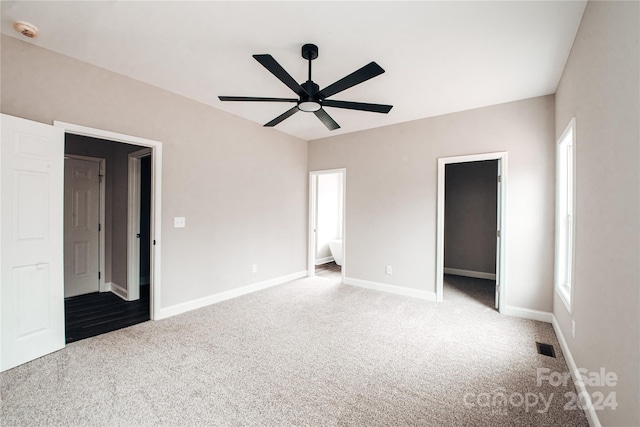 unfurnished bedroom with ceiling fan, a walk in closet, light carpet, and multiple windows