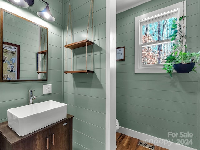 bathroom with hardwood / wood-style floors, vanity, toilet, and wooden walls