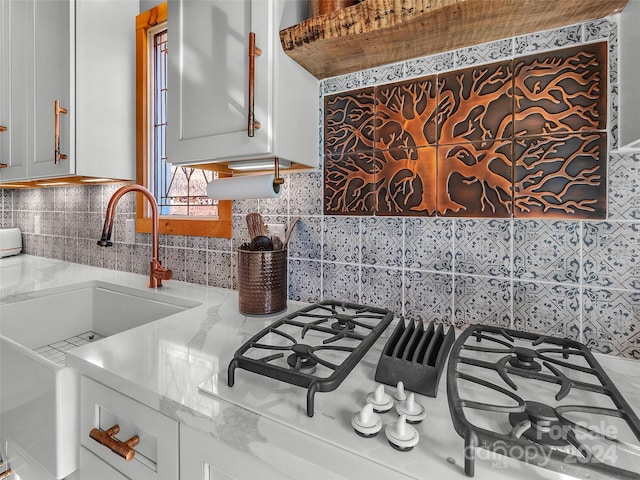 kitchen featuring white cabinetry, decorative backsplash, light stone countertops, and gas cooktop