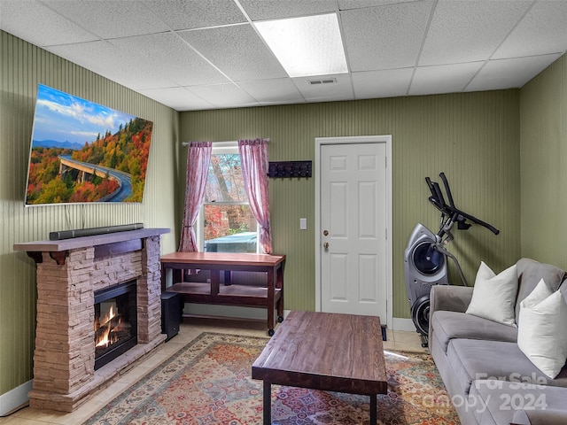 living room with a paneled ceiling, a stone fireplace, and light tile patterned floors