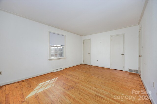 empty room featuring baseboard heating, crown molding, and light wood-type flooring