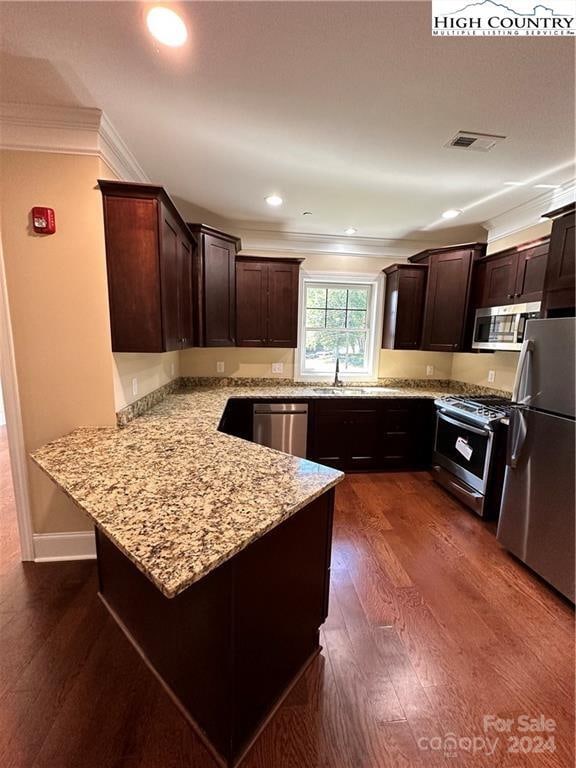 kitchen featuring kitchen peninsula, appliances with stainless steel finishes, light stone countertops, crown molding, and dark wood-type flooring