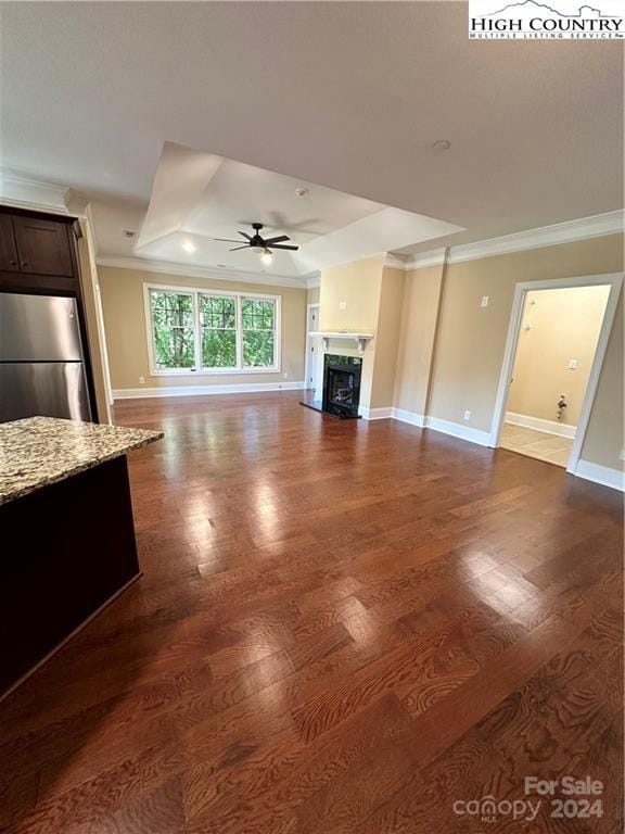 unfurnished living room featuring a tray ceiling, ceiling fan, wood-type flooring, and ornamental molding