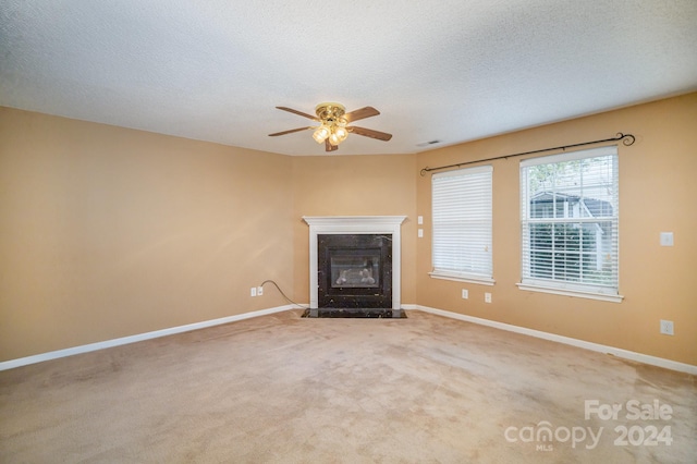 unfurnished living room with ceiling fan, light colored carpet, a textured ceiling, and a high end fireplace