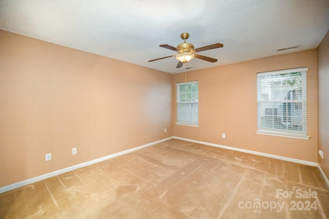 empty room with ceiling fan, light colored carpet, a textured ceiling, and a wealth of natural light