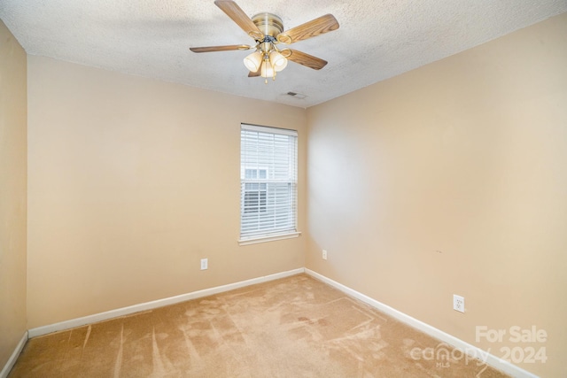 empty room with ceiling fan, light colored carpet, and a textured ceiling