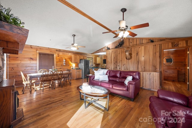 living room with a textured ceiling, vaulted ceiling, ceiling fan, wooden walls, and hardwood / wood-style flooring