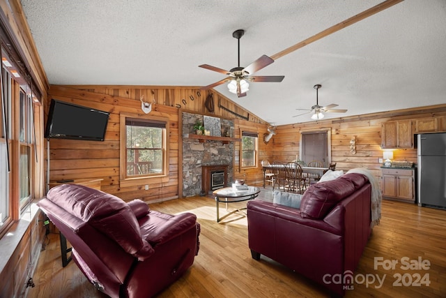 living room with a stone fireplace, wooden walls, light hardwood / wood-style flooring, ceiling fan, and a textured ceiling