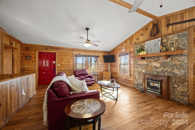 living room with hardwood / wood-style floors, wood walls, lofted ceiling with beams, ceiling fan, and a textured ceiling