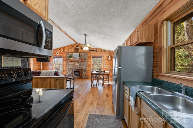 kitchen with appliances with stainless steel finishes, light wood-type flooring, a textured ceiling, and wooden walls