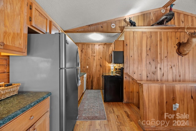 kitchen with wood walls, vaulted ceiling, light wood-type flooring, a textured ceiling, and appliances with stainless steel finishes