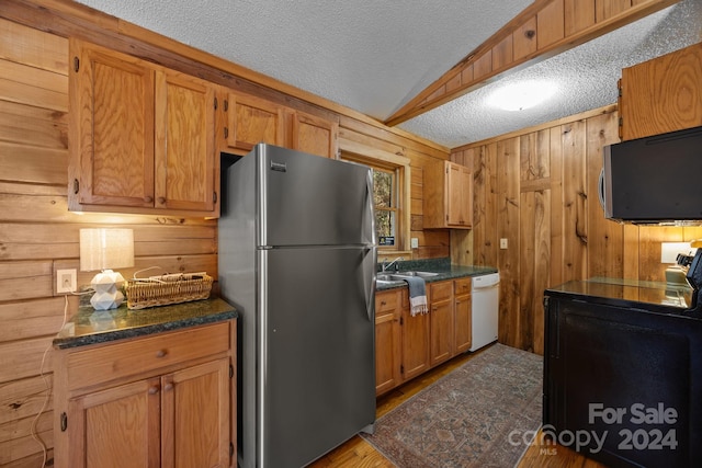 kitchen featuring vaulted ceiling, wood walls, a textured ceiling, and appliances with stainless steel finishes