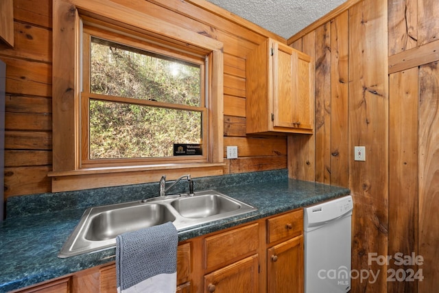 kitchen with dishwasher, a textured ceiling, sink, and wood walls