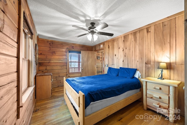 bedroom with ceiling fan, wooden walls, light hardwood / wood-style floors, and a textured ceiling