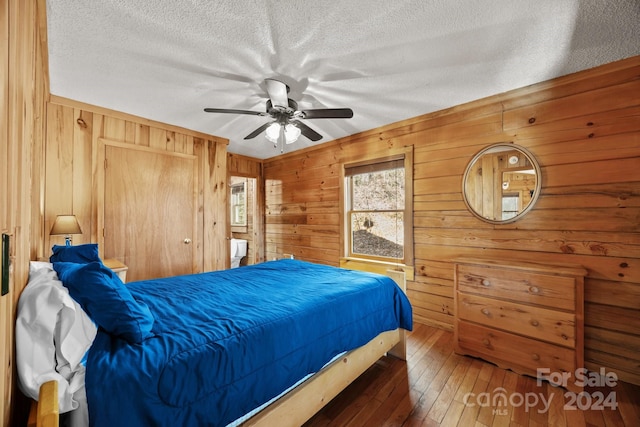 bedroom with ceiling fan, dark hardwood / wood-style flooring, a textured ceiling, and wooden walls