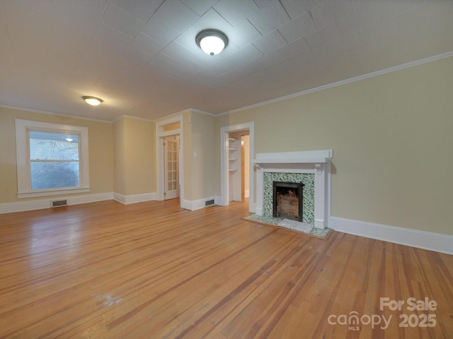 unfurnished living room featuring ornamental molding, a tiled fireplace, and light hardwood / wood-style flooring