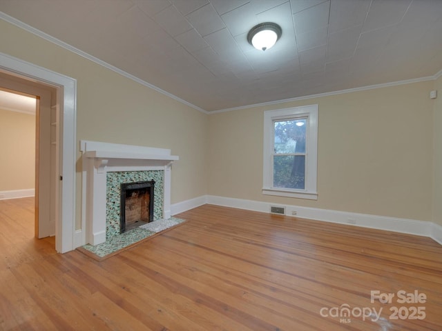 unfurnished living room with baseboards, wood finished floors, a tiled fireplace, and ornamental molding