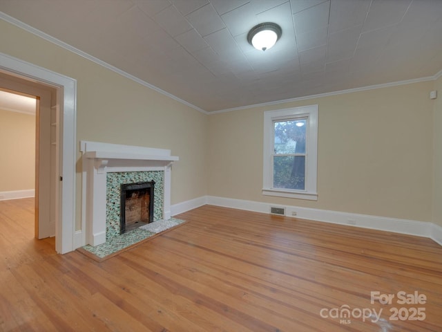 unfurnished living room with a tiled fireplace, crown molding, and light hardwood / wood-style flooring