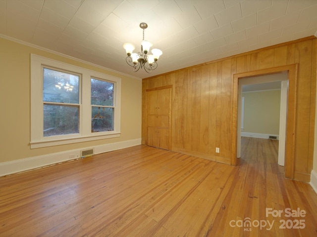 unfurnished dining area featuring an inviting chandelier, wooden walls, crown molding, and light hardwood / wood-style floors