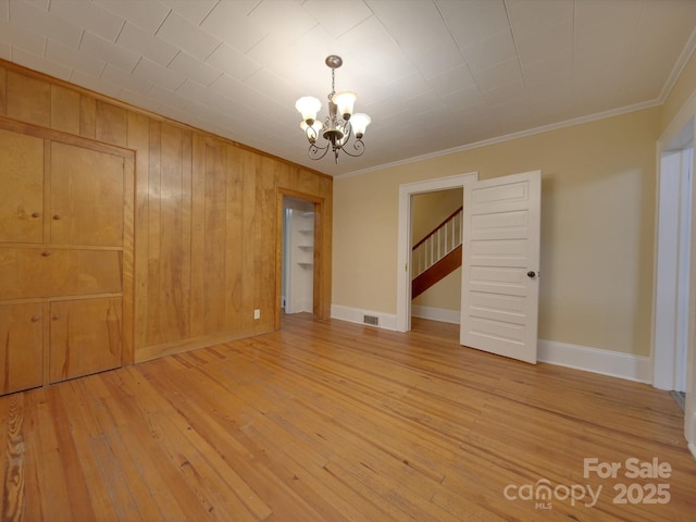 unfurnished room featuring an inviting chandelier, crown molding, wood-type flooring, and wood walls