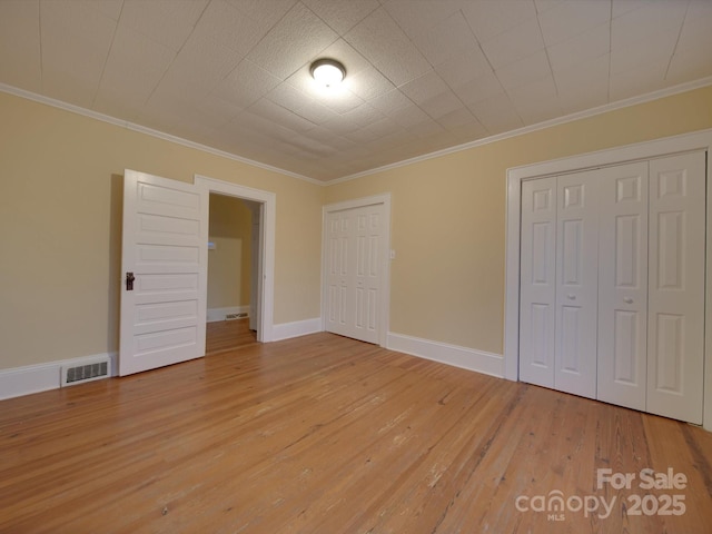 unfurnished bedroom with ornamental molding, light hardwood / wood-style floors, and multiple closets