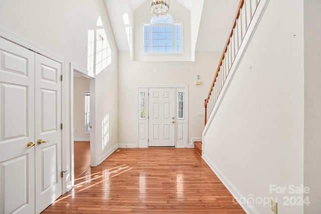 entryway featuring light wood-type flooring, high vaulted ceiling, and a chandelier