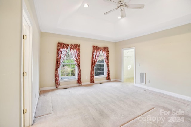 empty room featuring a raised ceiling, ceiling fan, light carpet, and ornamental molding