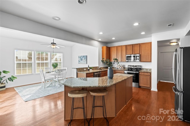 kitchen with dark wood-type flooring, a kitchen island, a breakfast bar, and appliances with stainless steel finishes