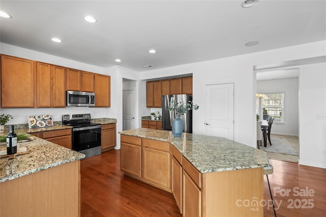 kitchen with stainless steel appliances, a kitchen island, dark wood-type flooring, and light stone counters