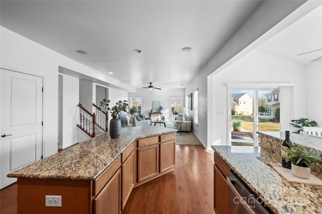 kitchen featuring dark wood-type flooring, ceiling fan, a center island, and light stone counters