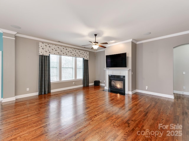 unfurnished living room featuring a glass covered fireplace, ornamental molding, arched walkways, and wood finished floors