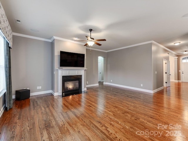 unfurnished living room featuring a glass covered fireplace, wood finished floors, ornamental molding, and ceiling fan