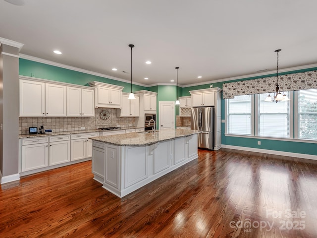 kitchen featuring appliances with stainless steel finishes, white cabinets, decorative light fixtures, and a kitchen island with sink