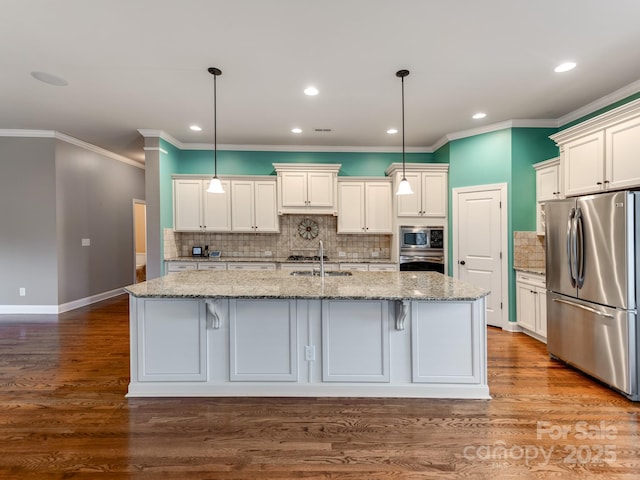 kitchen with hanging light fixtures, stainless steel appliances, a center island with sink, and light stone counters